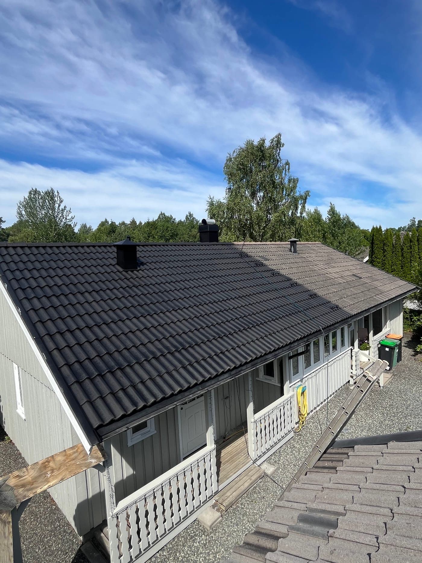 Ett tak under arbeid: venstre side ferdig vasket og malt svart, høyre side fortsatt med den gamle, slitte overflaten